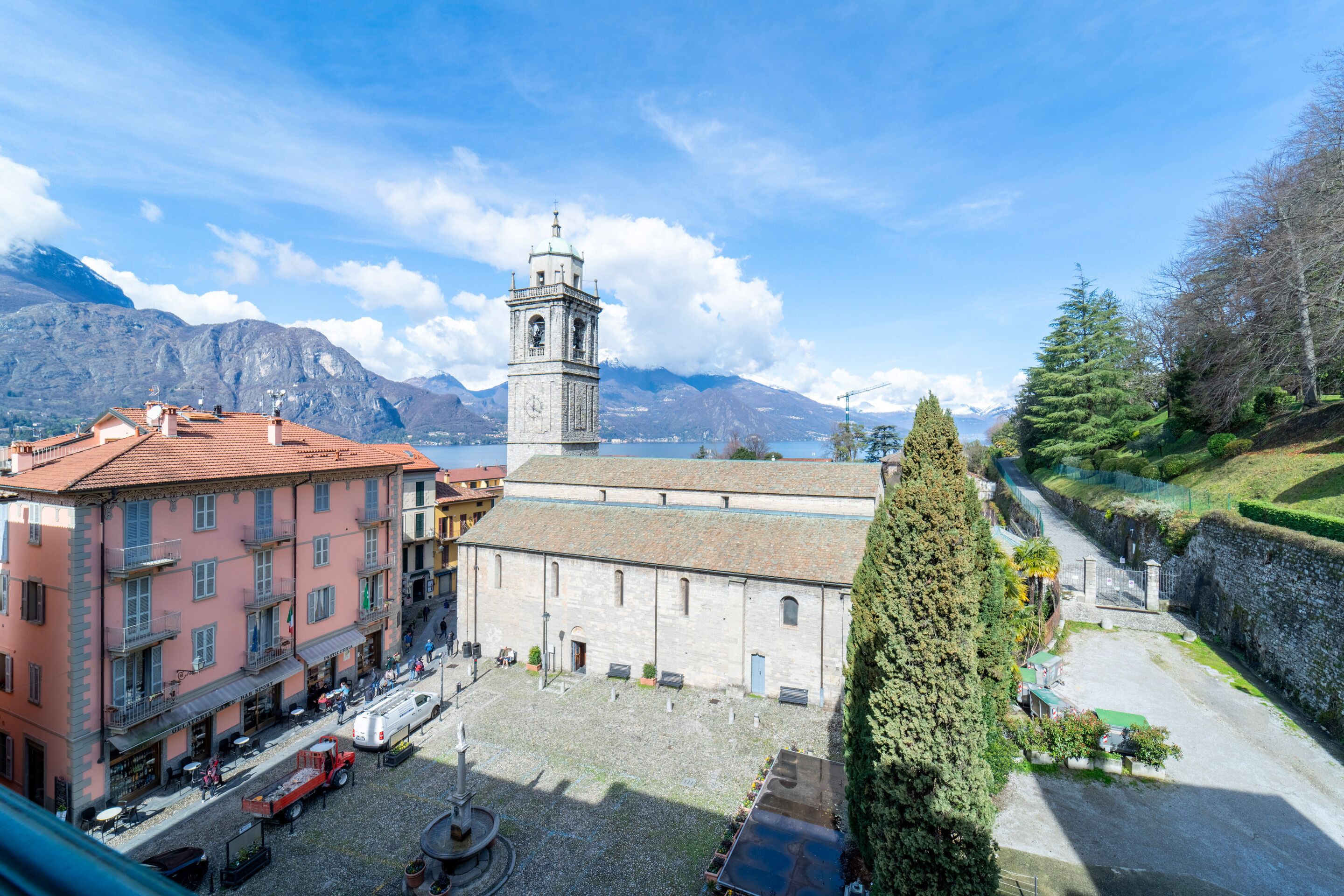 A courtyard with a bell tower, buildings with balconies, and a mountain backdrop.