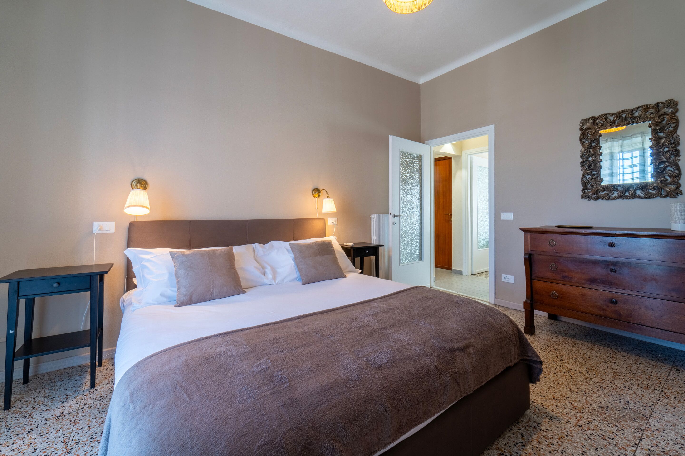 A bedroom with a large bed, two bedside lamps, a dresser, and a mirror on the wall.