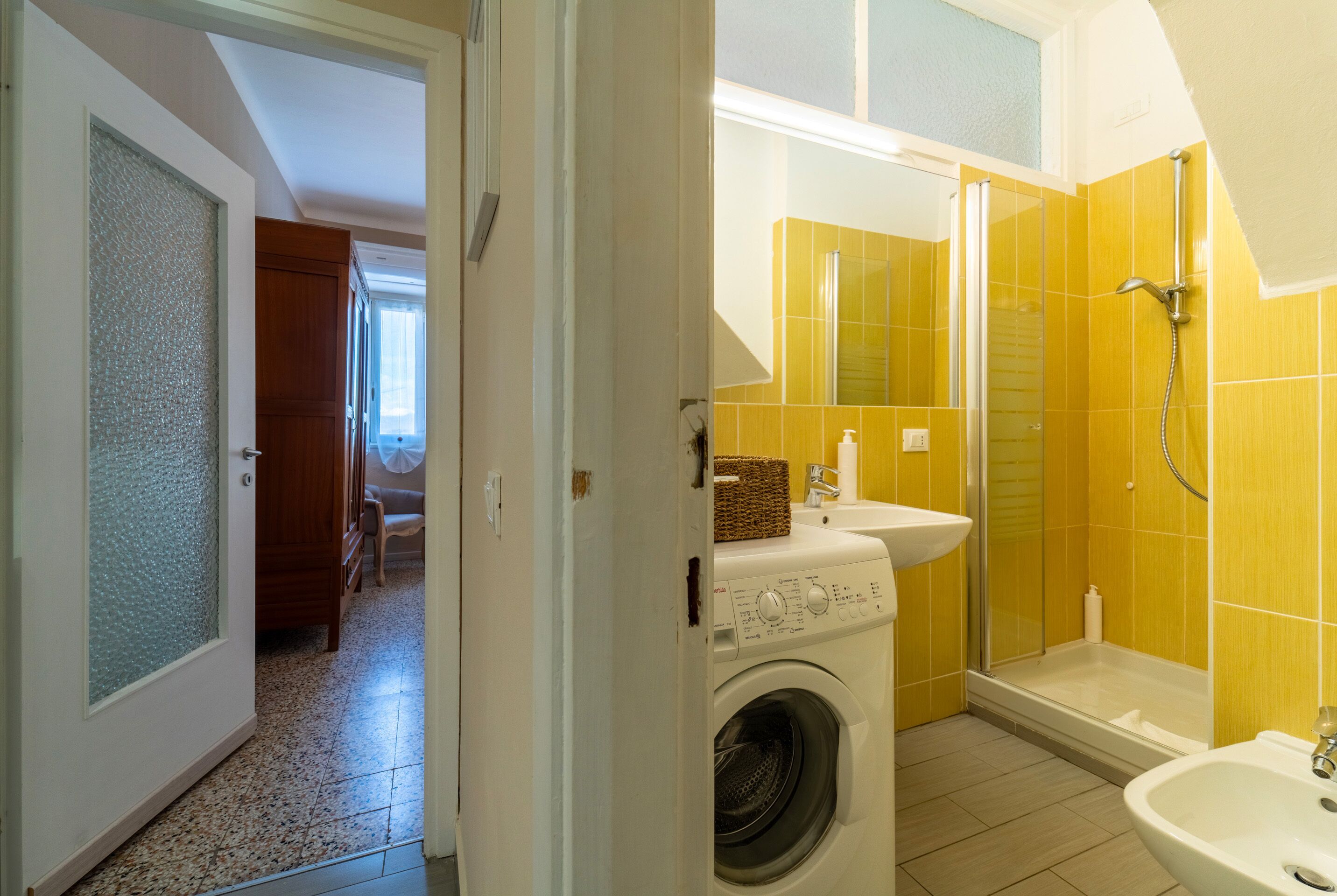 Une petite salle de bain comprenant un lave-linge, un lavabo et un espace douche.