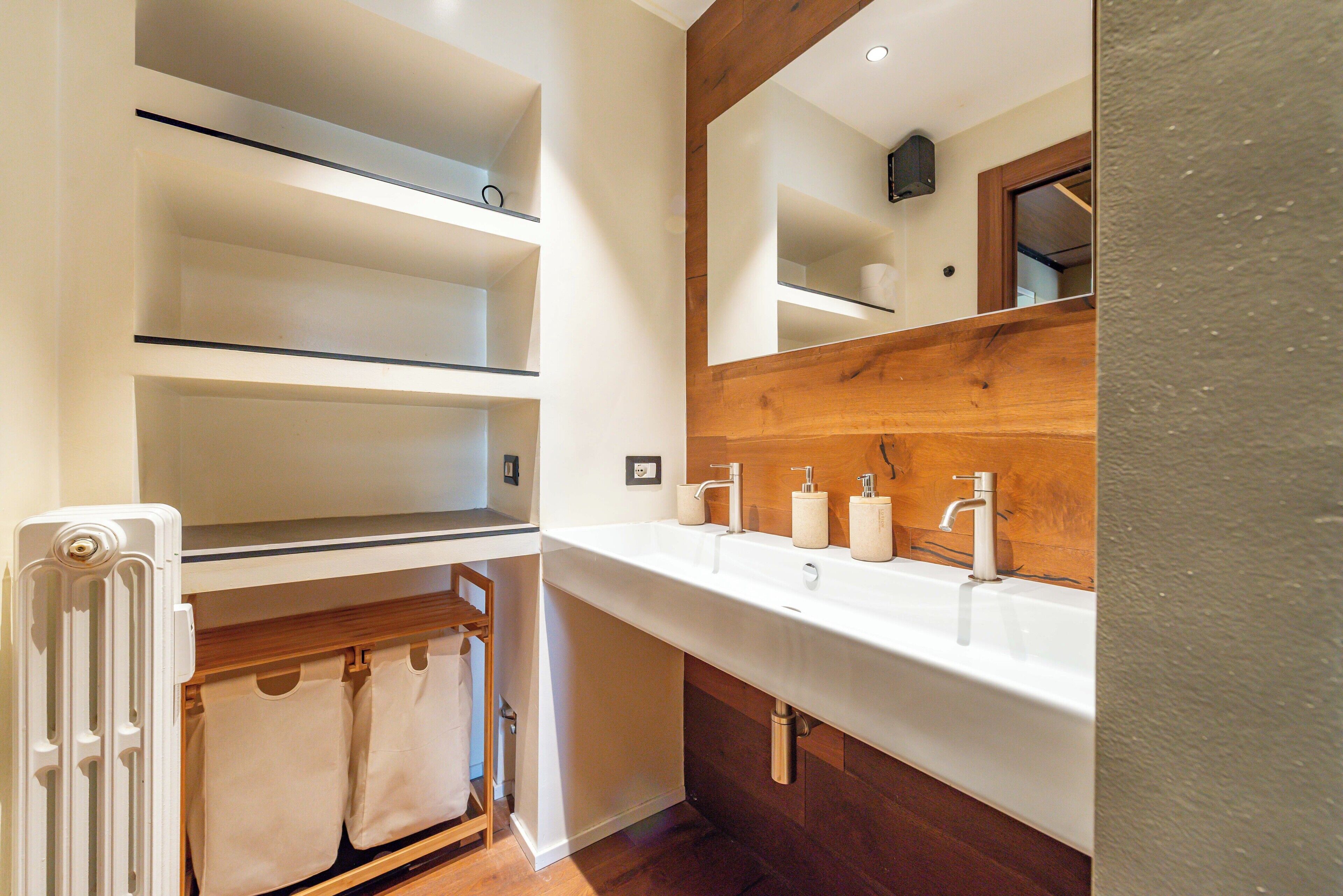 A modern bathroom with a large sink, wooden vanity, and built-in shelves.