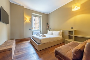 A bedroom with a bed, a sofa, a TV, a window, and a wall-mounted shelf. - Residenza Pasolini (Rome)