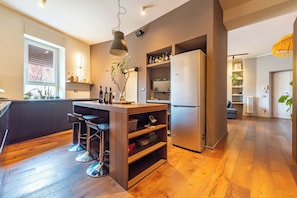 A modern kitchen with a central island, bar stools, a refrigerator, and wooden flooring. - Residenza Pasolini (Rome)