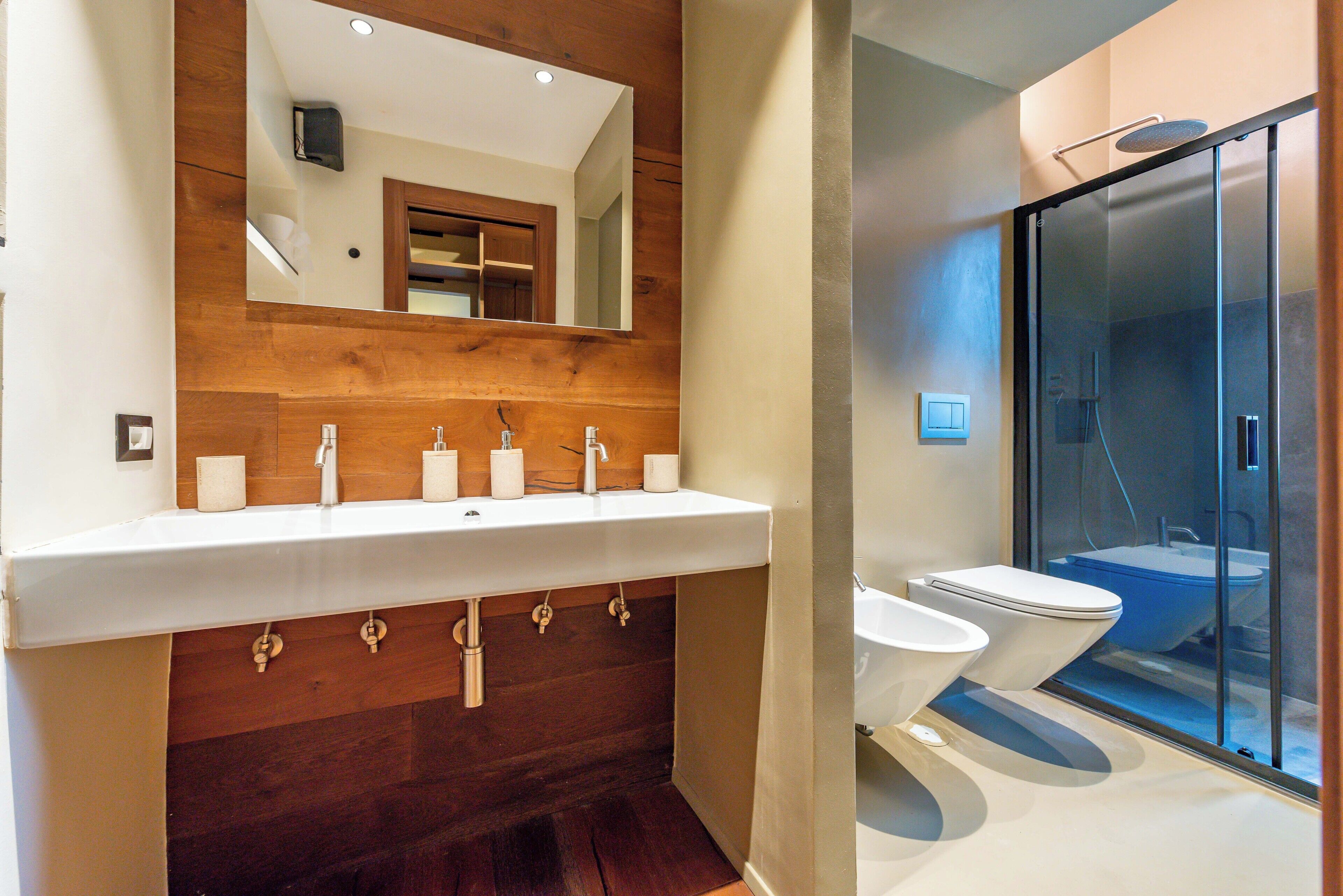 Un baño moderno con tocador de madera, un espejo grande y zona de ducha con mampara de vidrio.