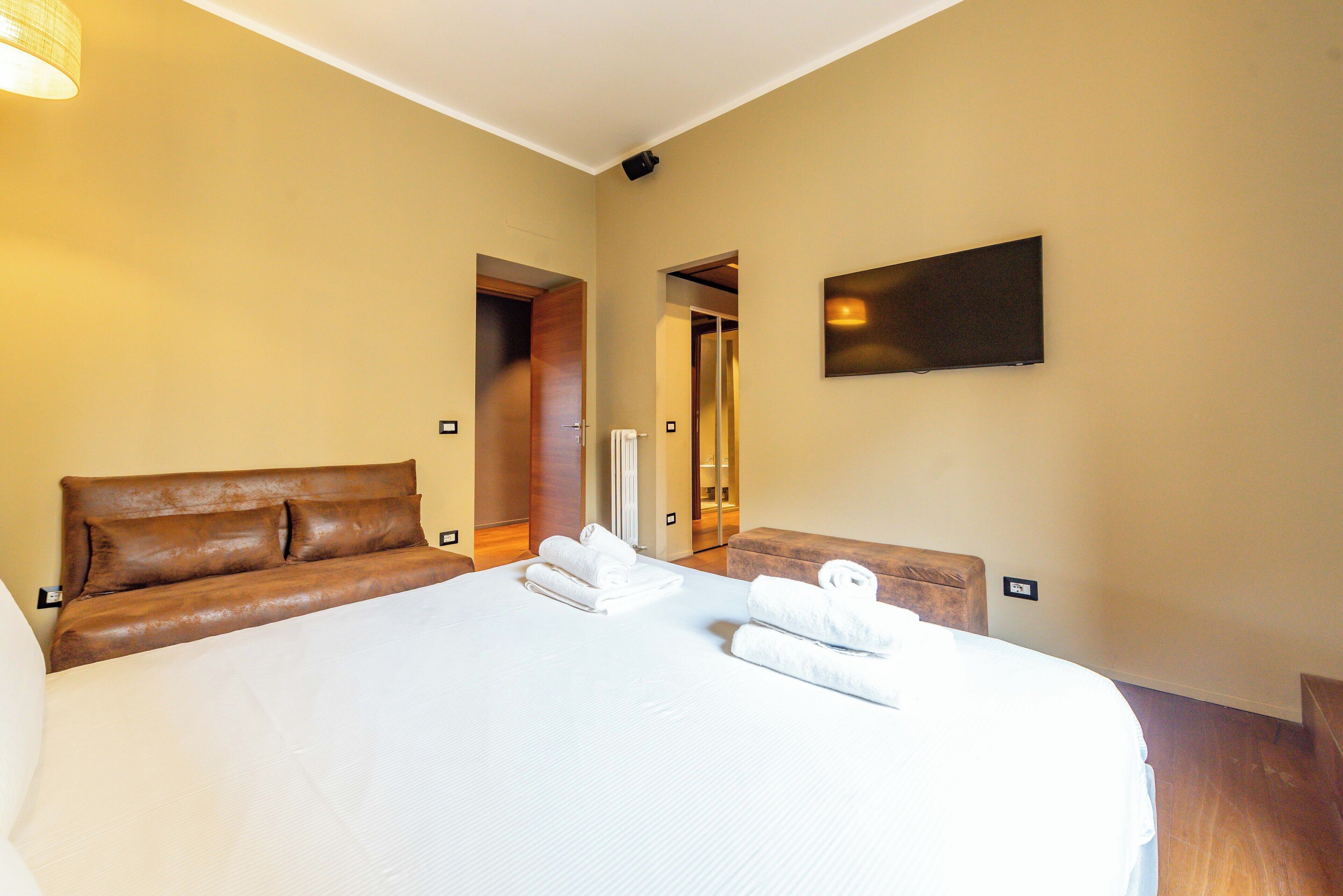 A hotel room with a large bed, a brown headboard, a flat-screen TV, and a mirror.