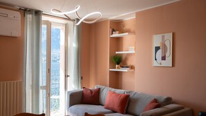 Een woonkamer met een bank, een eettafel en stoelen. Door een glazen deur is er uitzicht op zee.