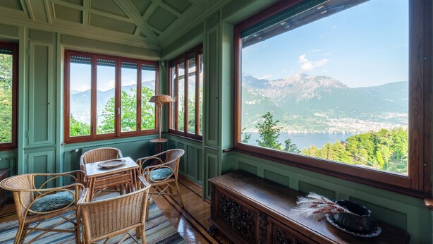 Ein Zimmer mit großem Fenster und Blick auf die Berge, einem Esstisch mit Korbstühlen und einer Holzbank mit Dekoration.