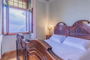 Ein Schlafzimmer mit einem Holzbett, einem Nachttisch mit Lampe und einem Fenster mit Vorhängen.