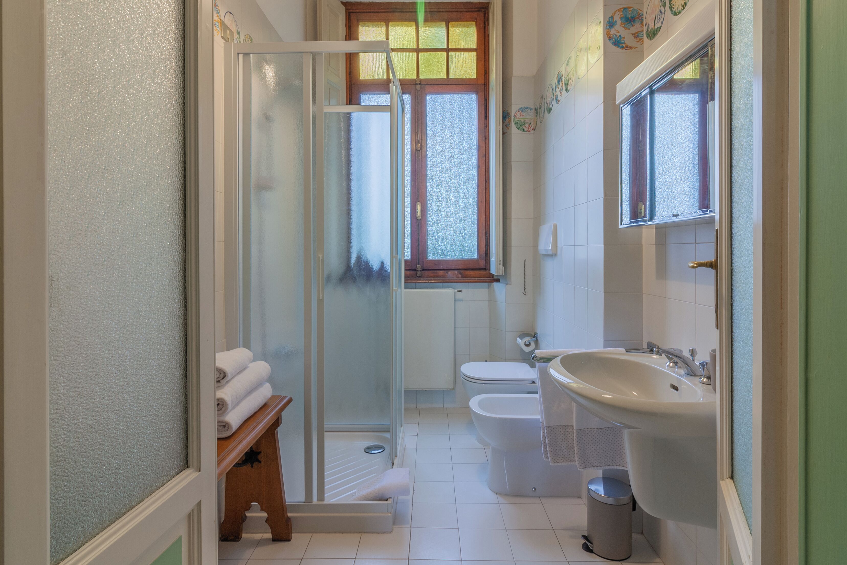 A bathroom with a glass shower enclosure, a toilet, a sink, and a small trash bin.