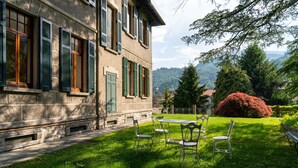 Ein Gebäude aus Stein mit grünen Fensterläden, einer grünen Rasenfläche und einem Tisch mit Stühlen.