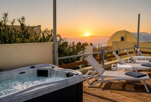 A rooftop terrace with a hot tub, lounge chairs, and a view of the sunset over the sea. - Sunset Horizon Oia (Santorini)