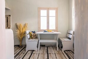 A small room with a white table and two chairs, a window, and a rustic wooden floor. - Sunset Horizon Oia (Santorini)