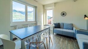 Una sala de estar moderna con comedor, ventanas amplias con vistas a la montaña, un sofá y una lámpara.