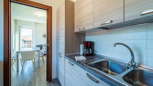 Una cocina moderna con lavamanos de acero inoxidable, armarios de madera y un área de comedor visible a través de una puerta abierta.