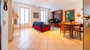 Una sala de estar con un sofá, una mesa de comedor con sillas, un televisor y una puerta.