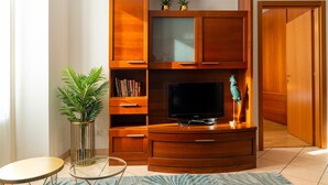 Una sala de estar con un aparador de madera, un televisor, una mesa de vidrio, una planta en maceta y una puerta.