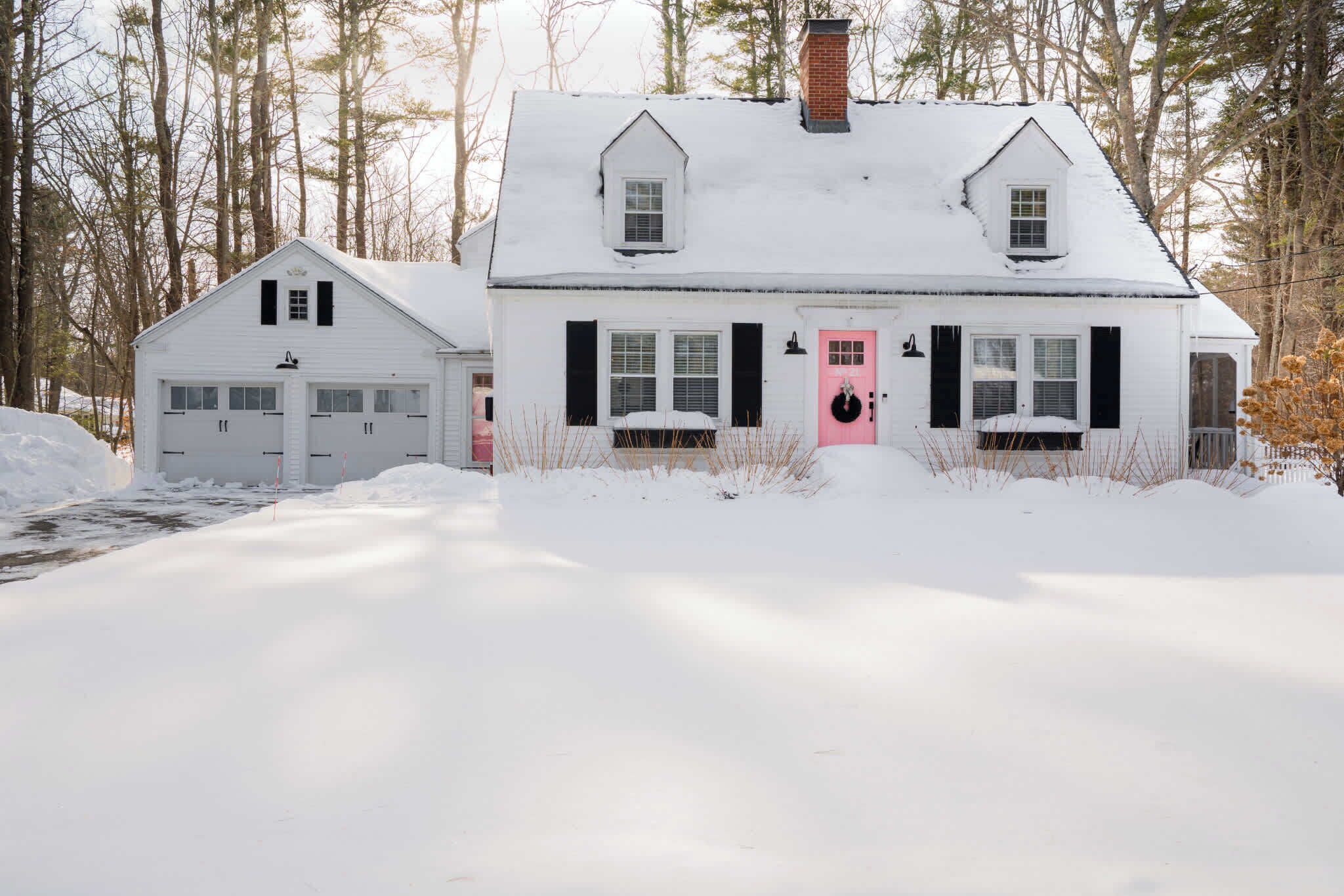 A snow-covered house with a pink door, two garage doors, and a chimney.