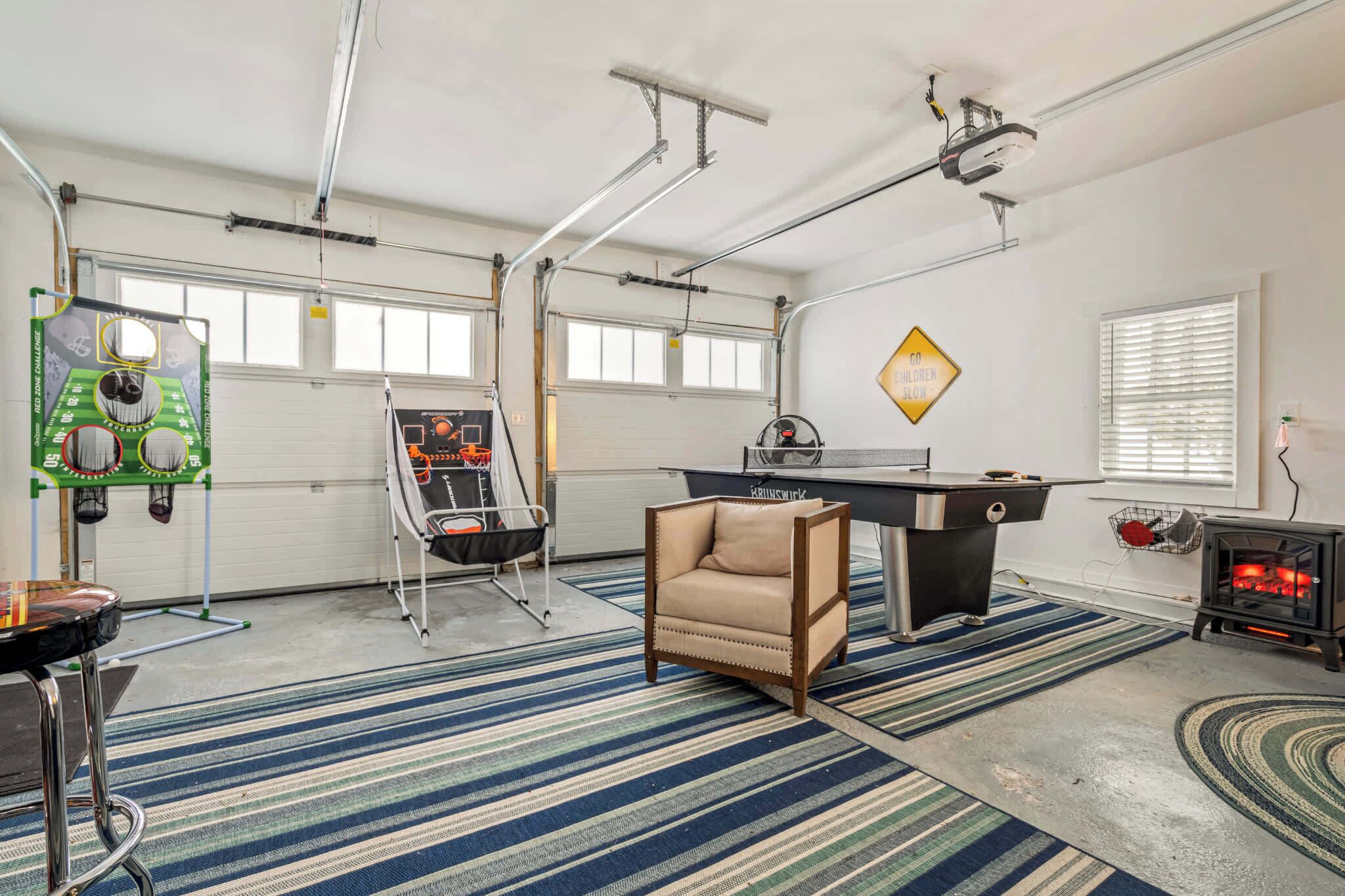 A spacious garage with a ping pong table, a comfortable chair, a pool table, and a wood-burning stove.