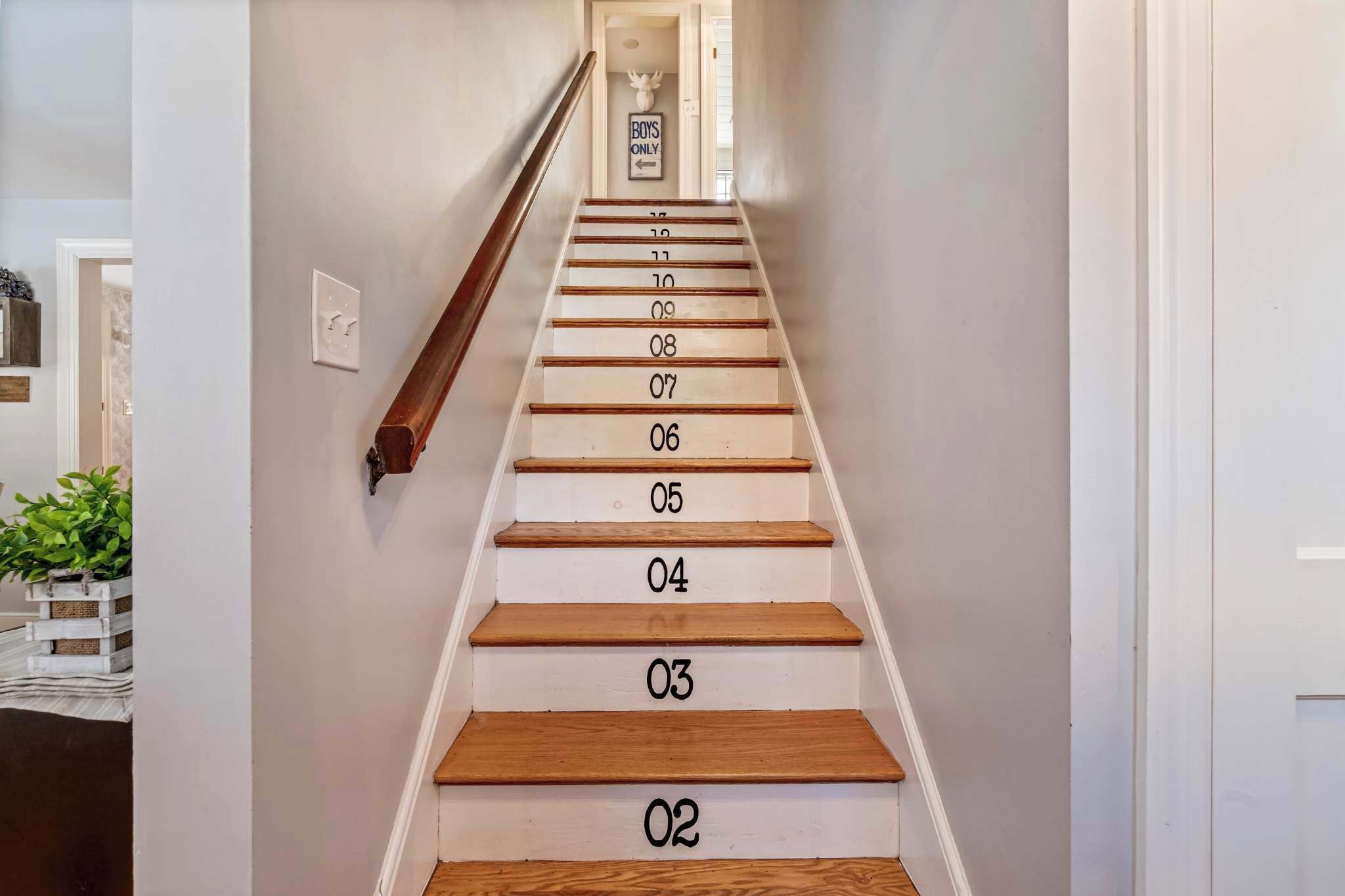 Un escalier avec des marches en bois et des murs blancs, menant à une porte sur laquelle est apposée une pancarte indiquant « Réservé aux garçons ».