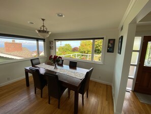 A dining area with a table, chairs, a vase with flowers, and a view of the sea through large windows. - North Beach Retreat Near Puget Sound (Seattle)