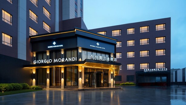 A modern hotel entrance with illuminated signage, a glass facade, and a well-lit driveway. - Giorgio Morandi Hotel - Bazhou (Langfang)
