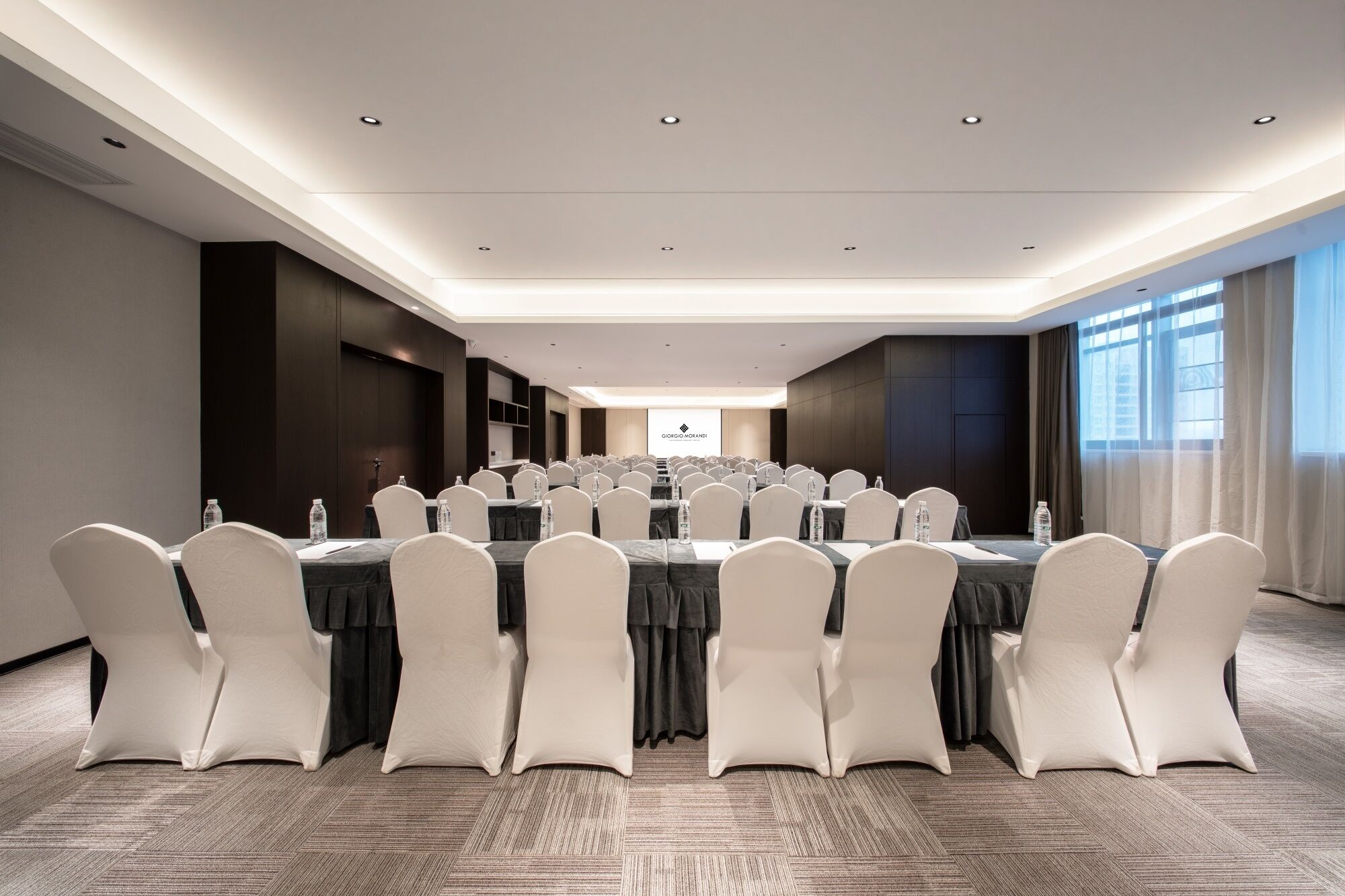 A conference room with tables, chairs, and a projector screen.