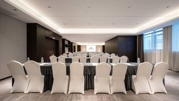 A conference room with tables, chairs, and a projector screen.