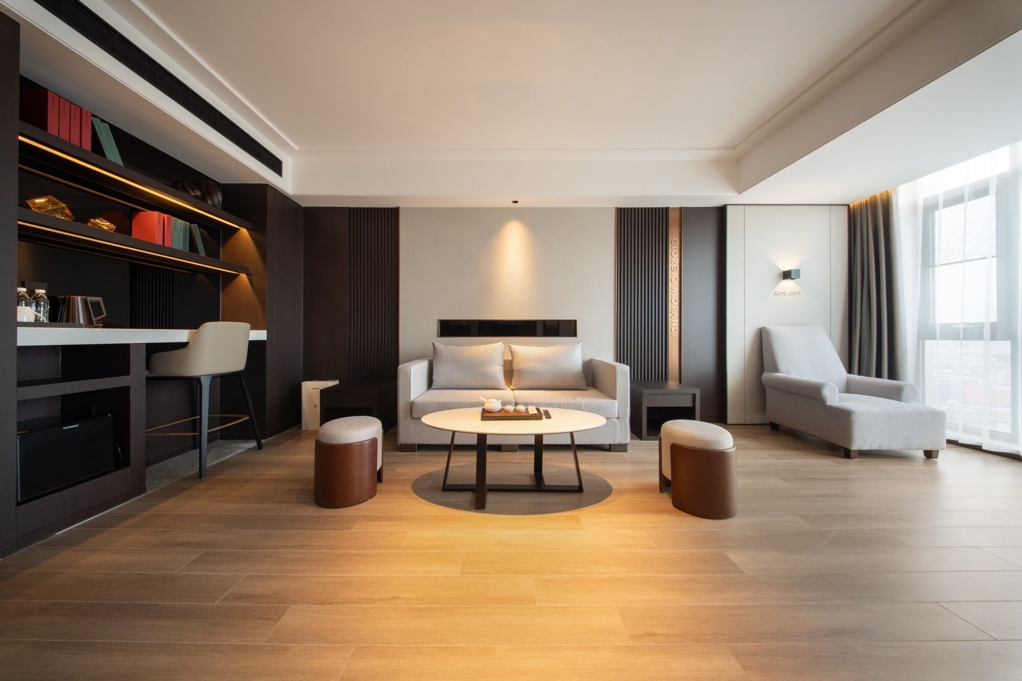 Una sala de estar moderna con sofá, mesa de centro y reposapiés, una estantería y un ventanal con cortinas.