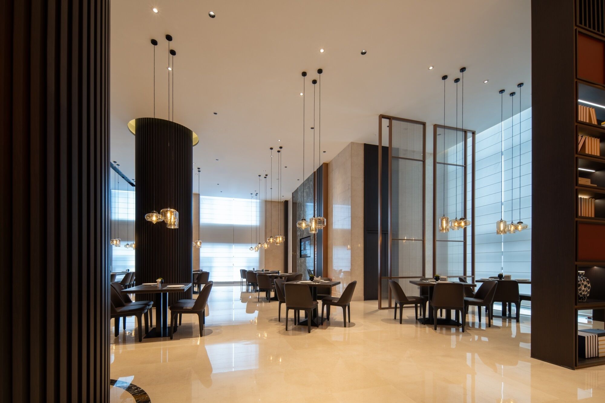 A modern interior with tables and chairs, pendant lighting, and a large window.