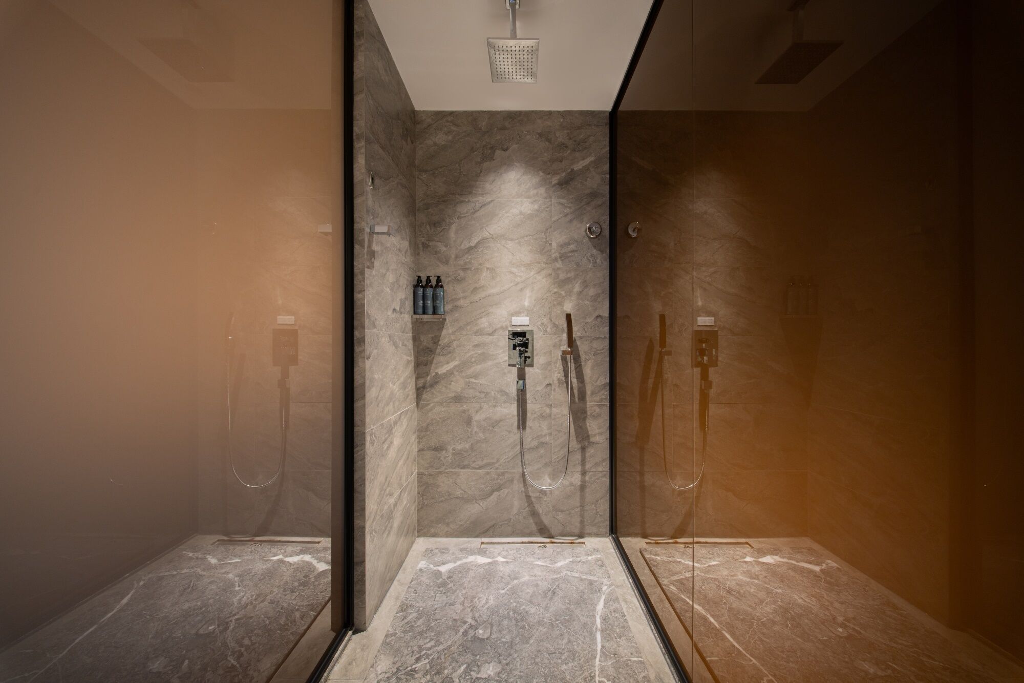 A modern bathroom with a glass-enclosed shower, marble walls, and a wooden floor.