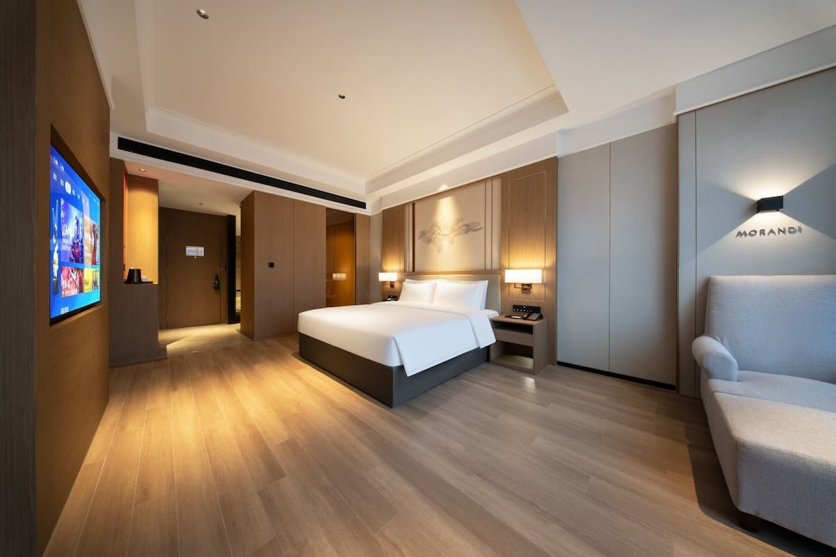 Una habitación de hotel moderna con una cama grande, mesitas de noche, una zona de estar y un televisor mostrando un menú.