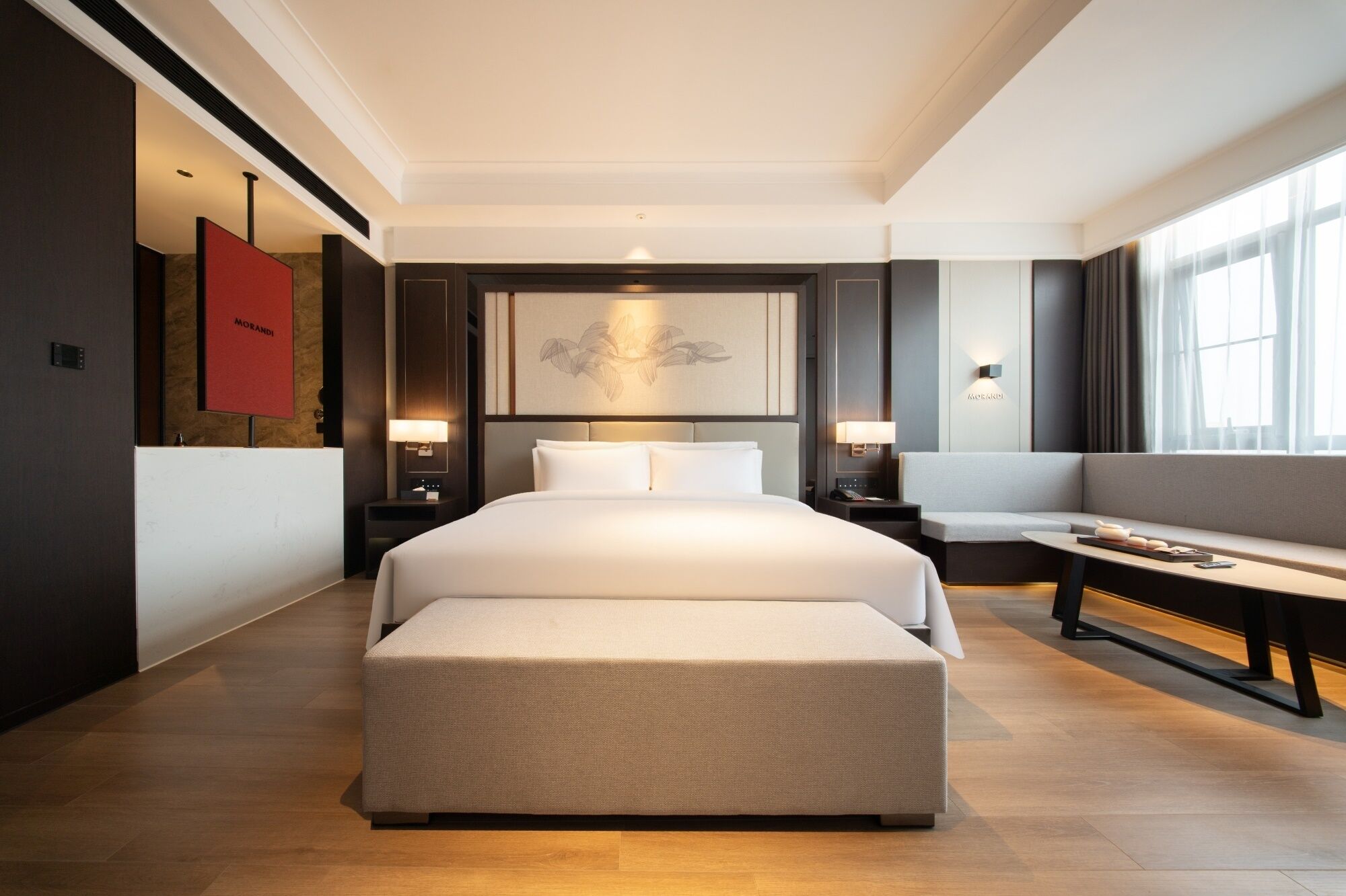 A hotel room with a large bed, a bench, a small table, and a wall-mounted TV.