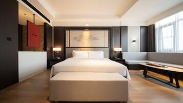 A hotel room with a large bed, a bench, a small table, and a wall-mounted TV.