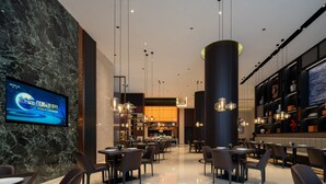A modern hotel lobby with a marble wall, a television displaying 'WORLD EXPRESS,' and a seating area with tables and chairs. - Giorgio Morandi Hotel - Bazhou (Langfang)