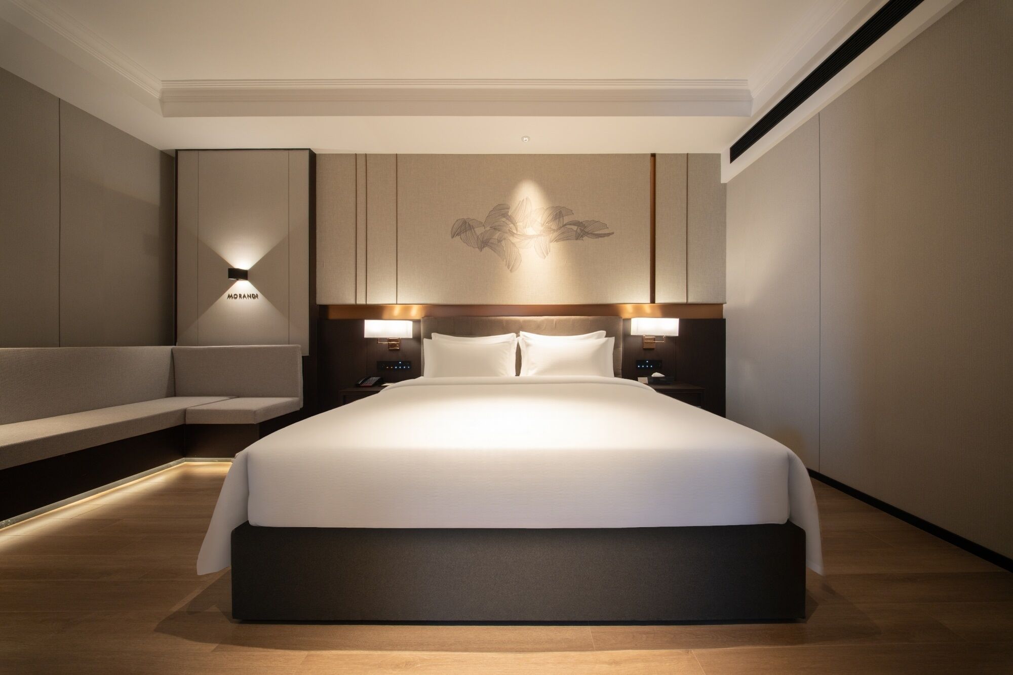 Una habitación de hotel moderna con una cama grande, lámparas de noche, un banco y una lámpara fijada a la pared.