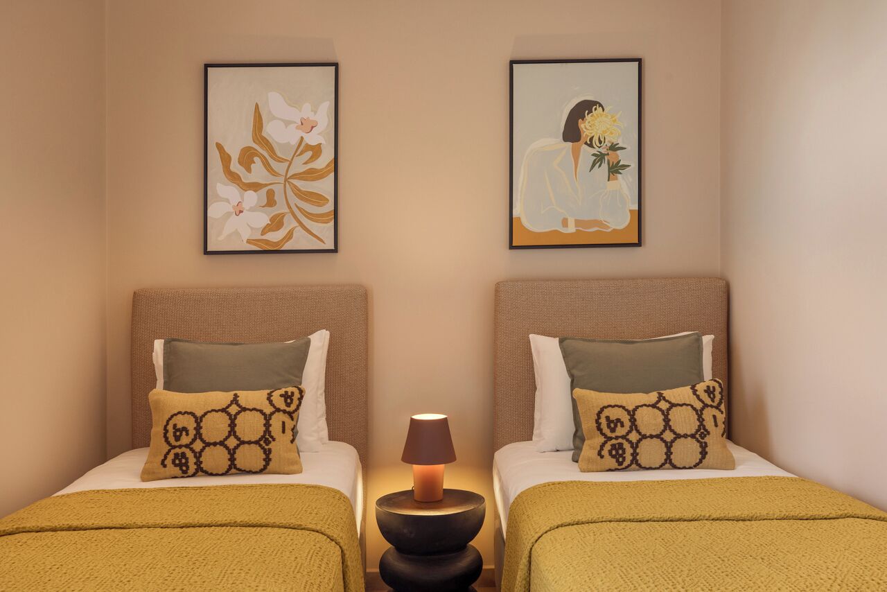 A hotel room with two beds, a bedside lamp, and two framed artworks on the wall.