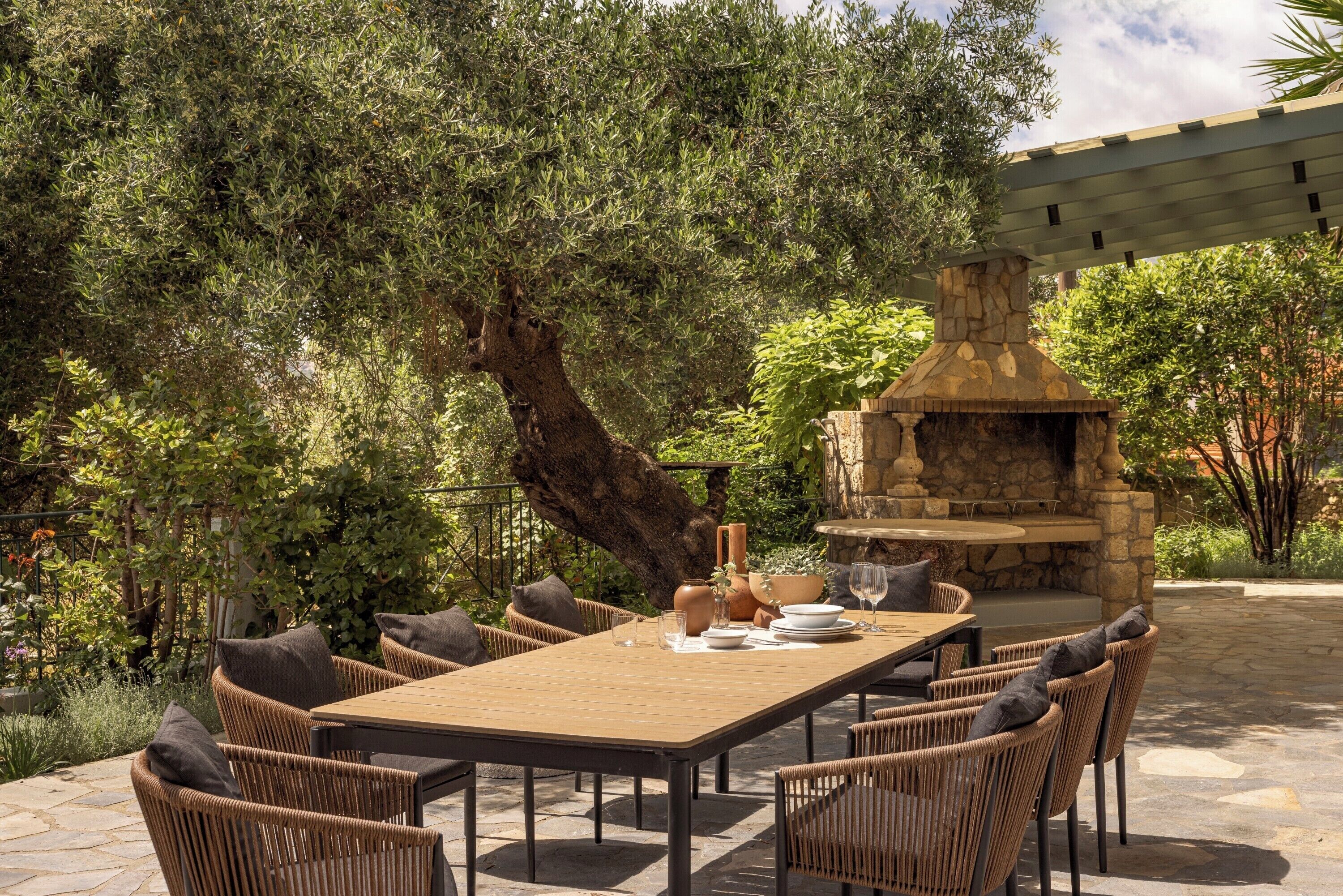 An outdoor dining area with a stone-built barbecue, wicker chairs, and a table set for four.