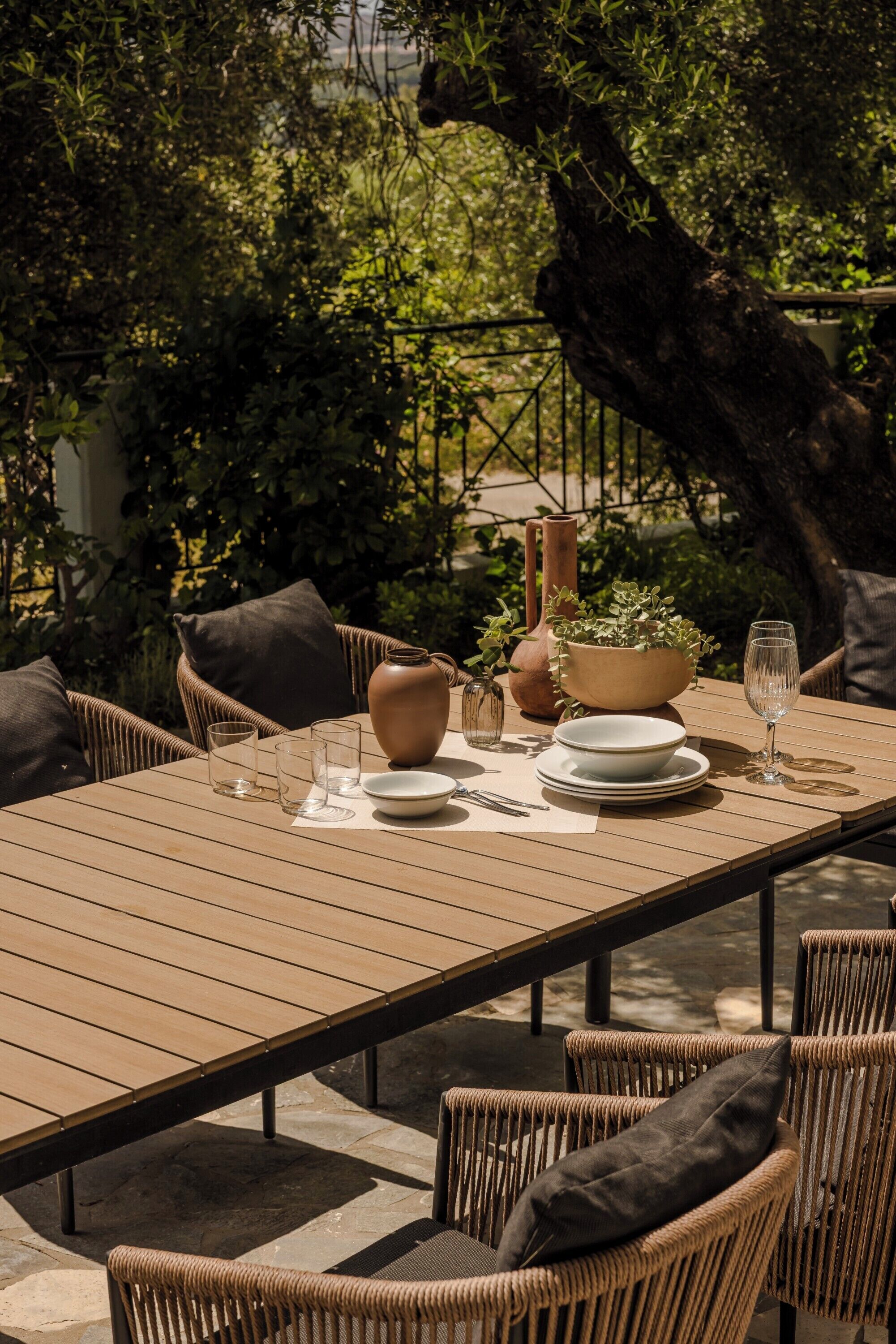 Una mesa de comedor al aire libre con sillas de mimbre, un florero, un tazón y una copa de vino.
