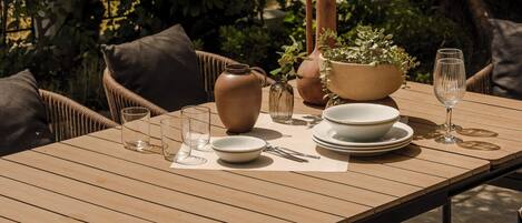Una mesa de comedor al aire libre con sillas de mimbre, un florero, un tazón y una copa de vino.