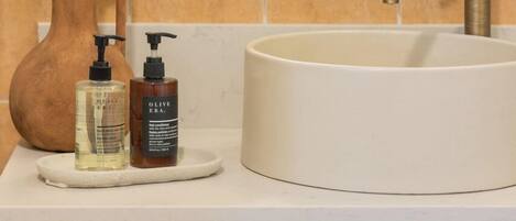 A bathroom with a round mirror, a white sink, and two bottles of lotion on a white countertop.