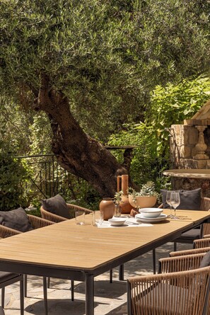 Un'area pranzo all'aperto con un tavolo lungo, sedie in vimini e un muro in pietra sullo sfondo.