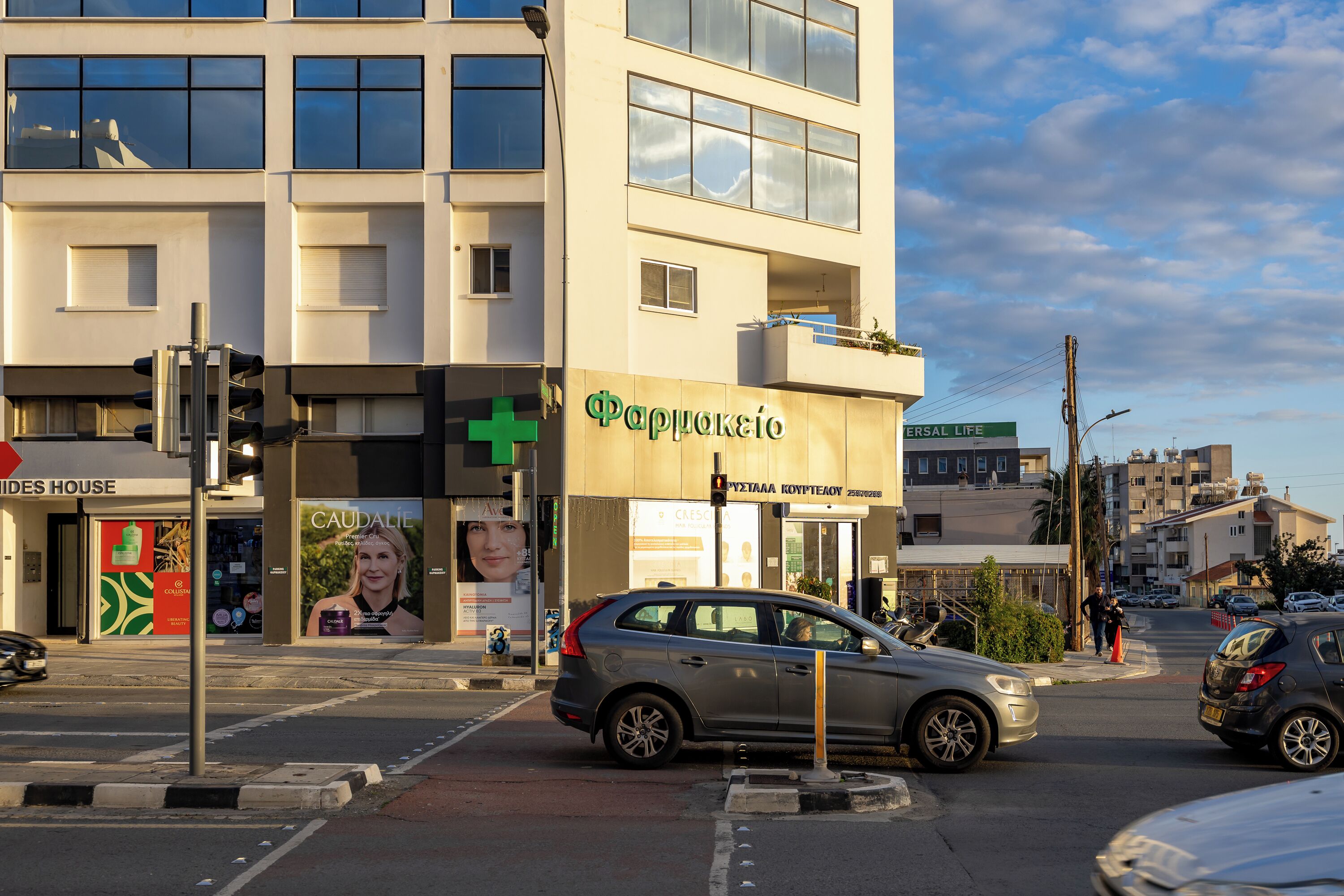 Ein Gebäude mit einer Apotheke, einem sichtbaren Eingang und einer Straßenecke mit Autos und Fußgängern.