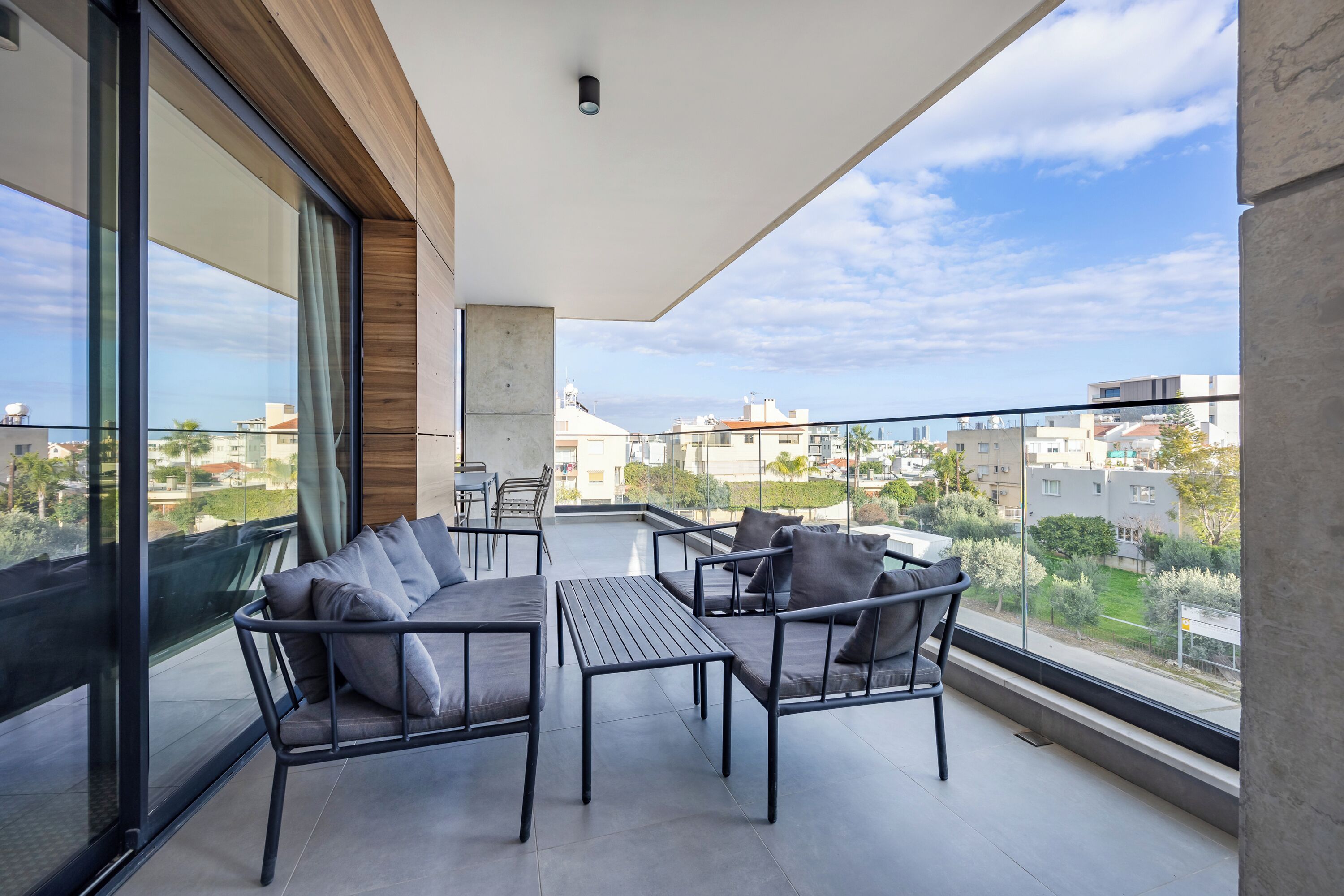 A balcony with a sofa, chairs, and a table, overlooking a residential area.