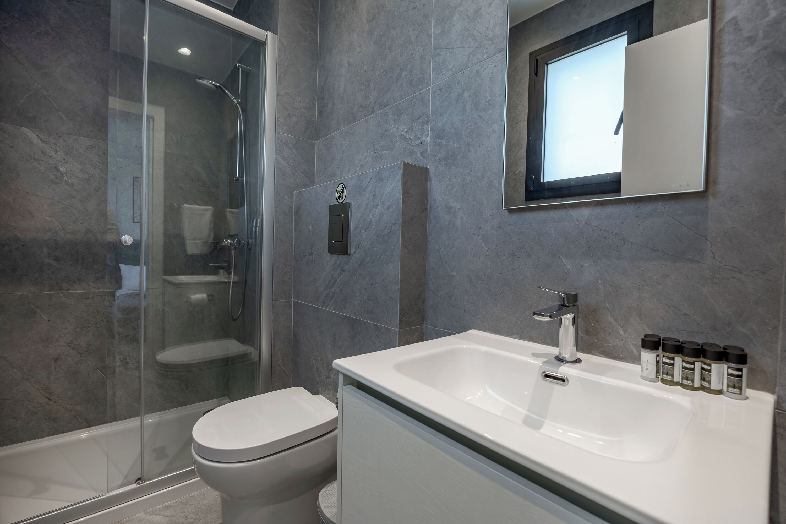 Une salle de bain moderne avec une douche à parois de verre, des toilettes blanches et un grand lavabo surmonté d’un miroir.