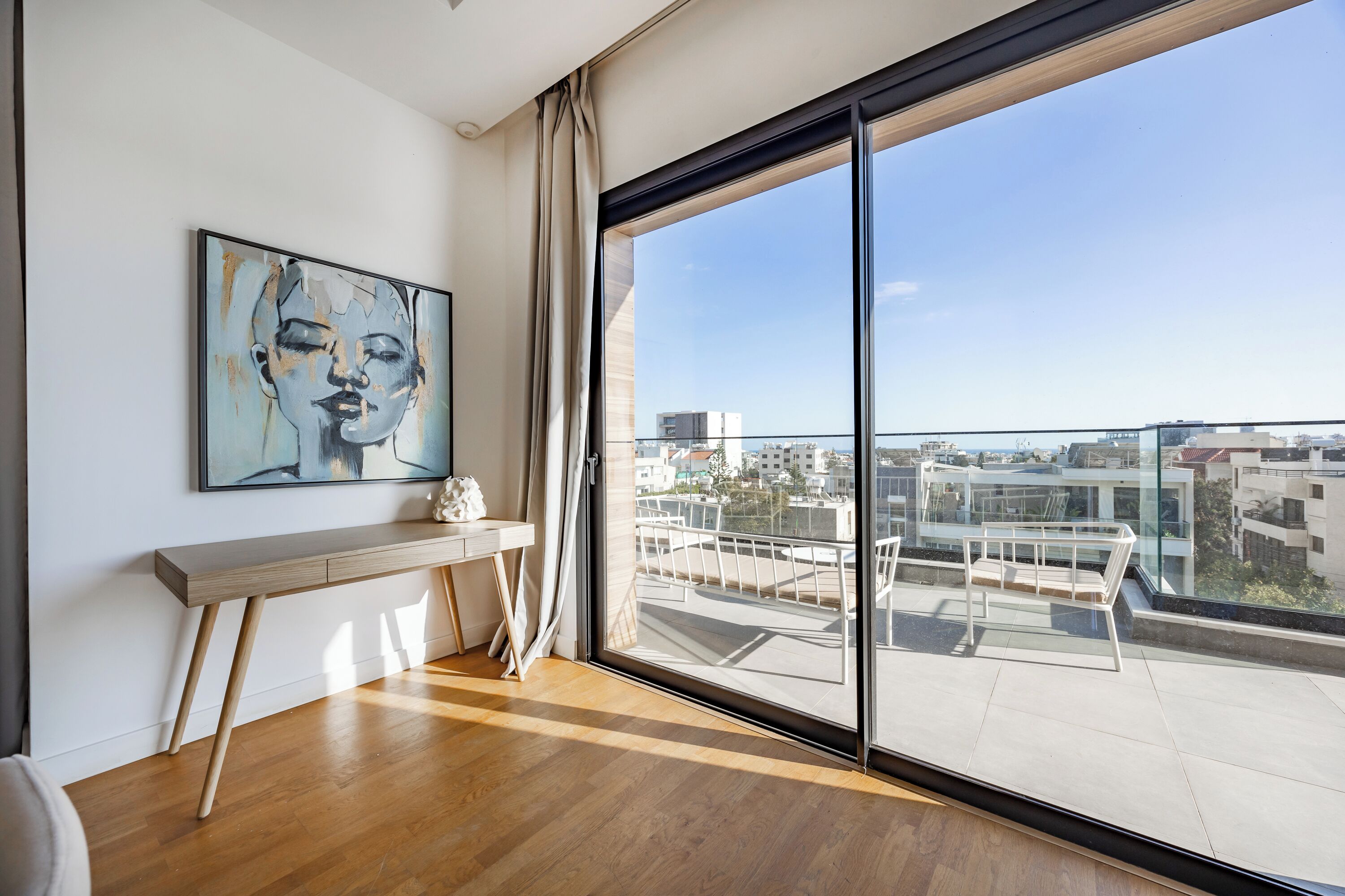 A modern room with a large window, a console table, and a painting on the wall.