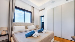 Moderni hotellihuone, jossa on suuri sänky, yöpöytä, verhoilla varustettu ikkuna ja vaatekaappi.