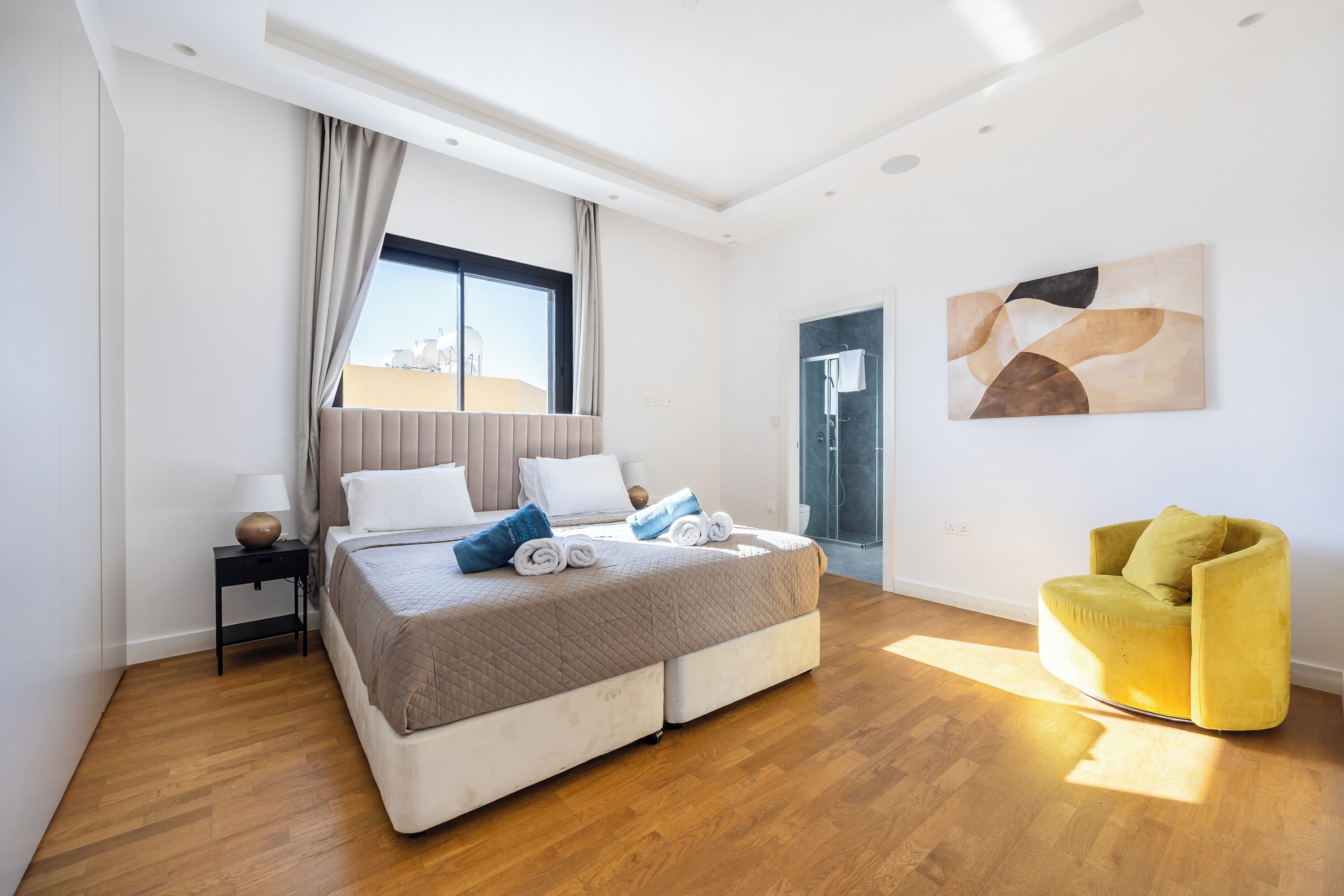 A modern bedroom with a bed, a chair, a window, and a painting on the wall.