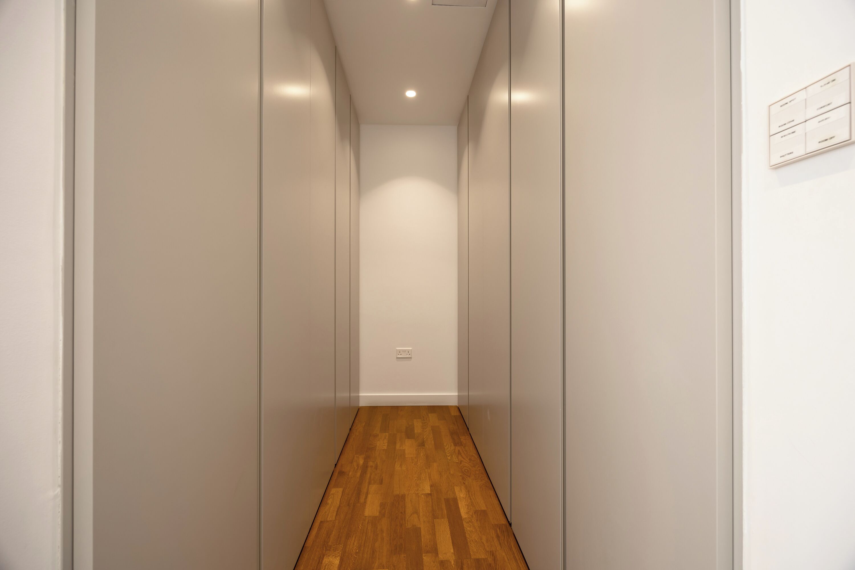 Un couloir étroit avec un plancher en bois et des murs blancs.