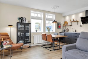 A modern living room with a sofa, a dining table with chairs, a bookshelf, and a kitchen area with a TV and shelves. - Nice two Bedroom, Downtown Apartment With Balcony (Akureyri)
