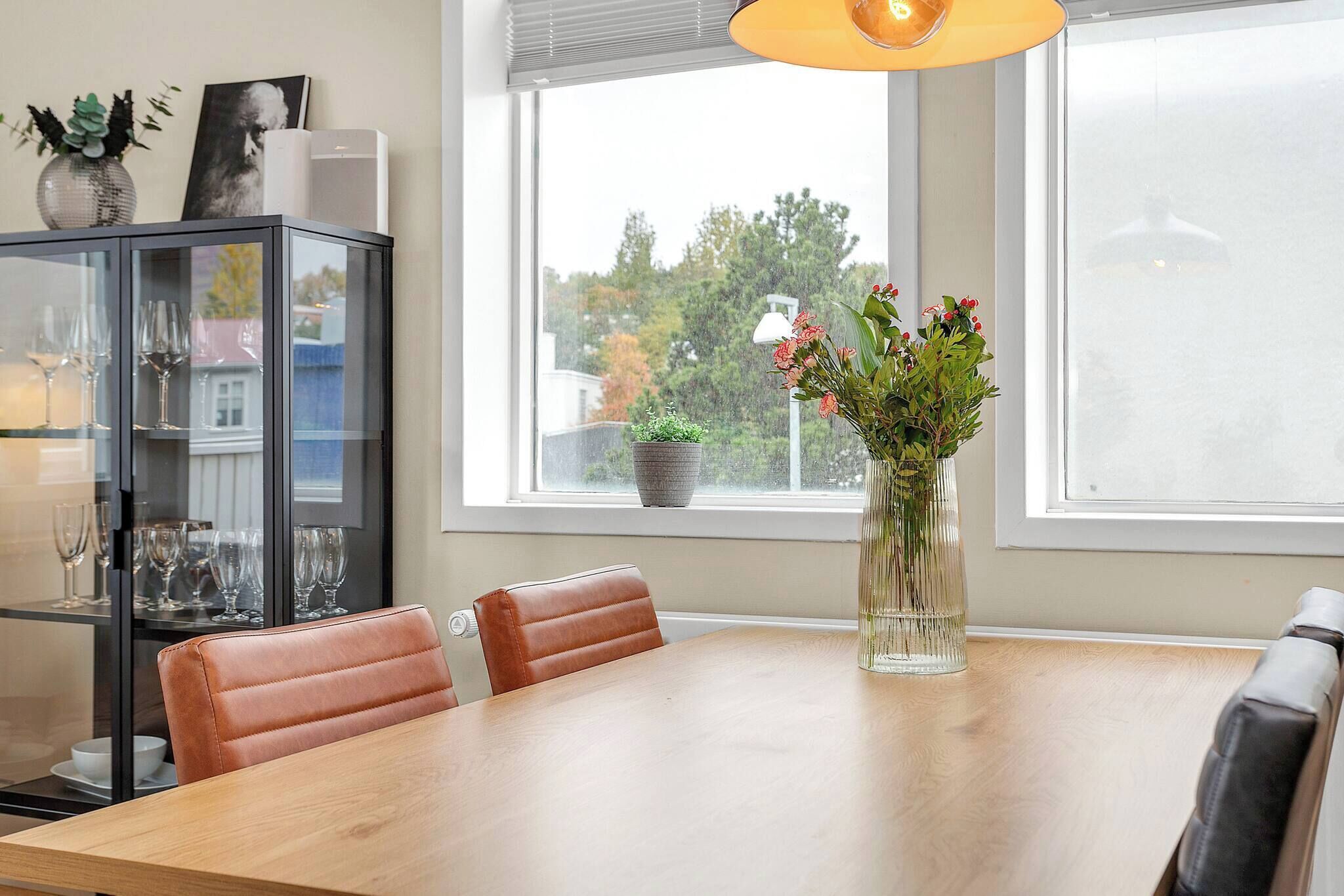 Un comedor con una mesa de madera, sillas de cuero, un aparador de vidrio con adornos y un jarrón con flores.