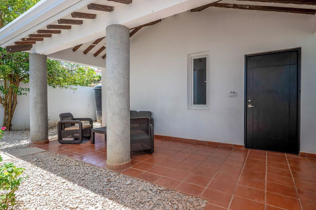 Área de varanda coberta com duas colunas, uma porta e assentos externos.